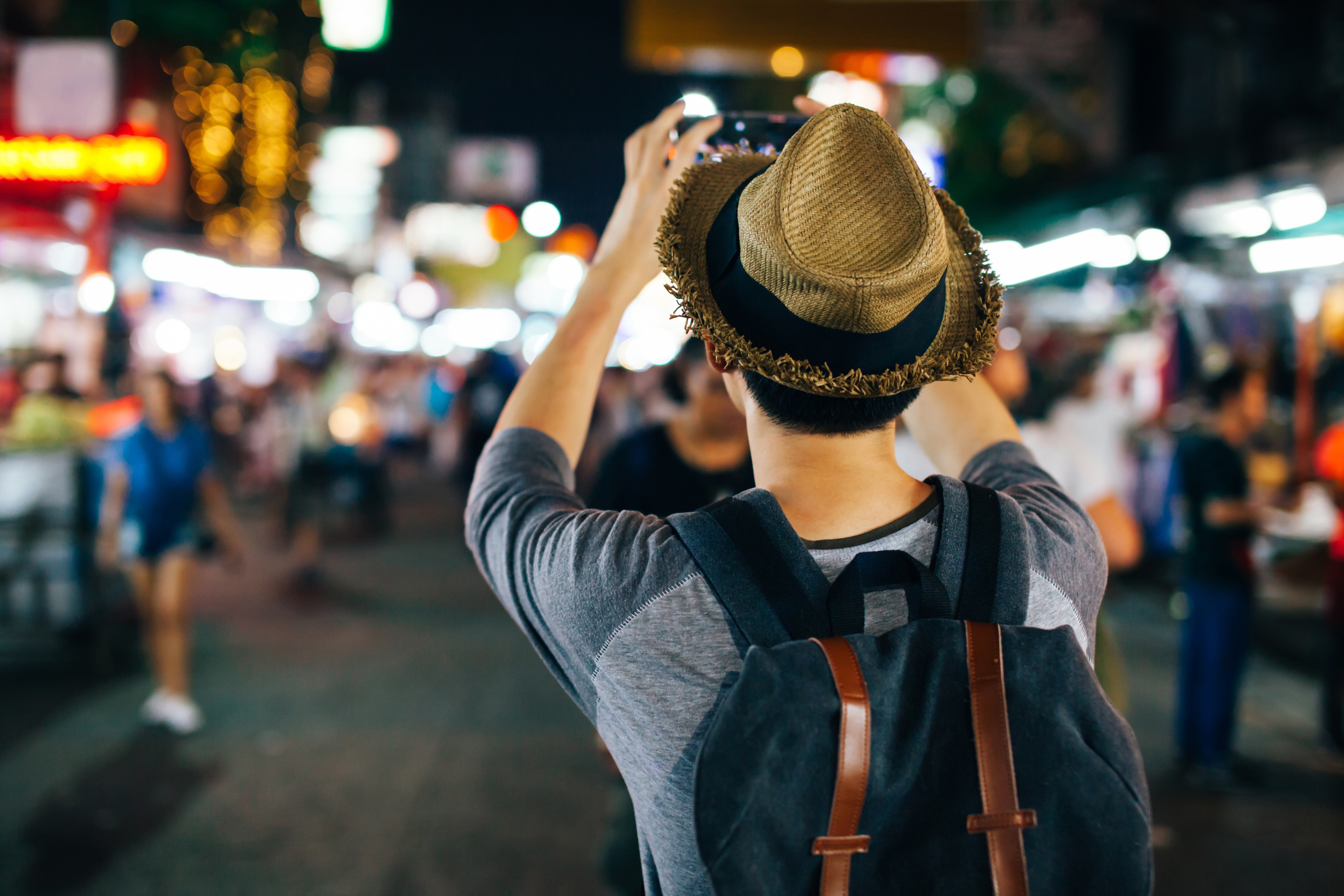 Young Asian traveler taking photo with mobile phone in Khaosan road at night in Bangkok, Thailand