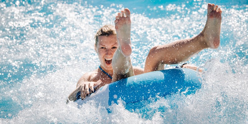 Funny girl taking a fast water ride on a float splashing water. Summer vacation with water park concept.